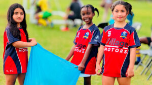 Three young girls in soccer gear help clean up.